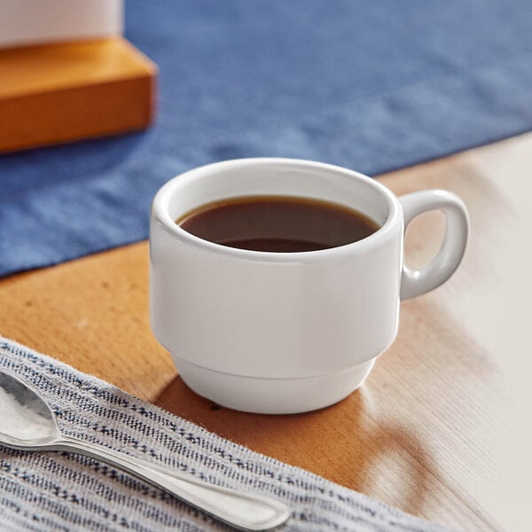 A stackable bright white stoneware espresso cup on a table with a cloth and a fork.