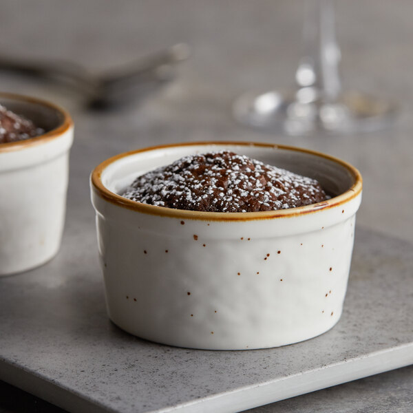 Two Acopa Keystone vanilla bean stoneware ramekins filled with chocolate pudding on a table.