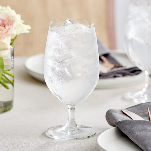 An Acopa Covella glass of water with ice and a flower on a table.