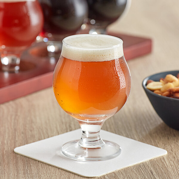 An Acopa Belgian beer tasting glass full of beer sits on a table with chips.