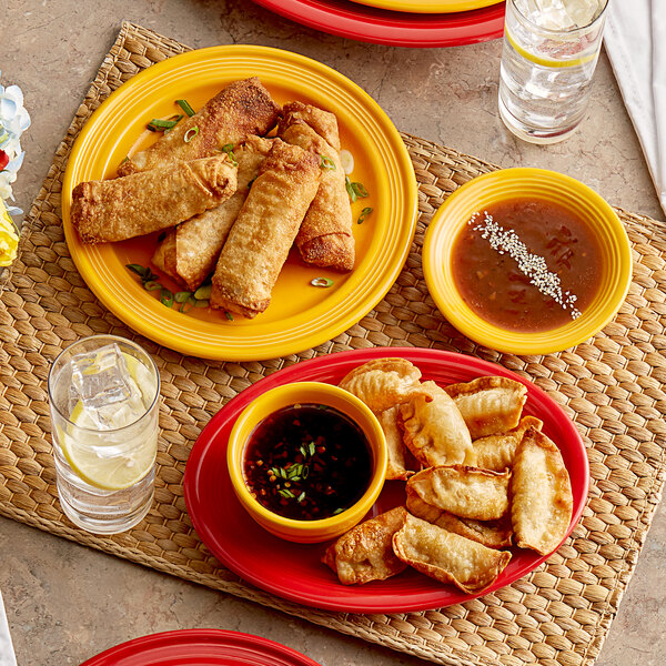 An Acopa Capri mango orange stoneware fruit bowl on a table with a plate of fried dumplings and dipping sauce.