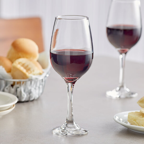 A table with a wine glass of red wine and a plate of food.