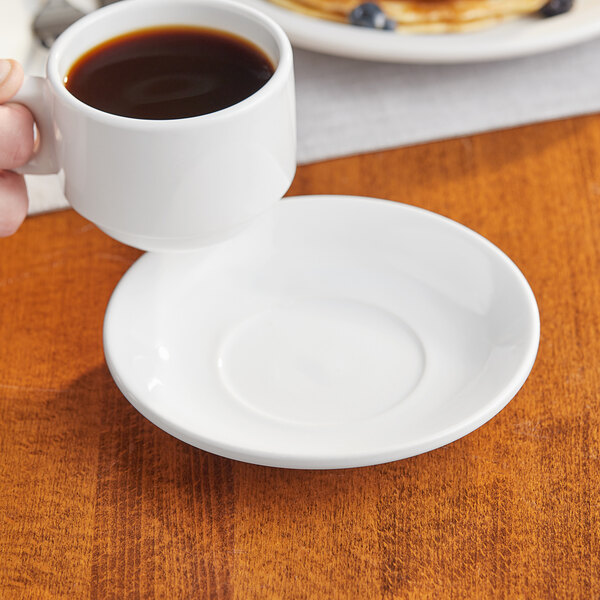 A hand holding a cup of coffee on a white Acopa saucer.