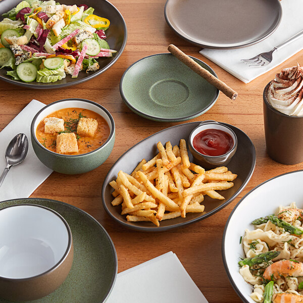 A brown matte stoneware cup filled with a whipped cream-topped beverage, shown alongside various dishes on a wooden table.