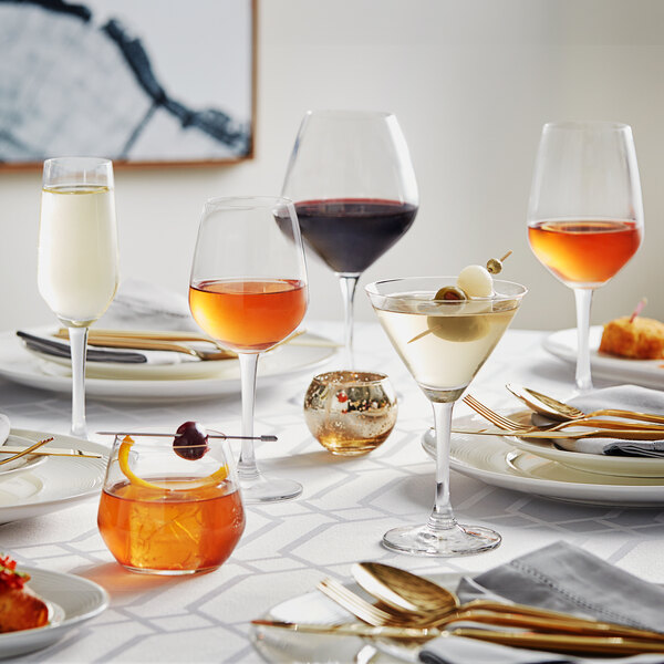 A close up of an Acopa Radiance martini glass filled with a yellow-orange cocktail with a cherry on top.