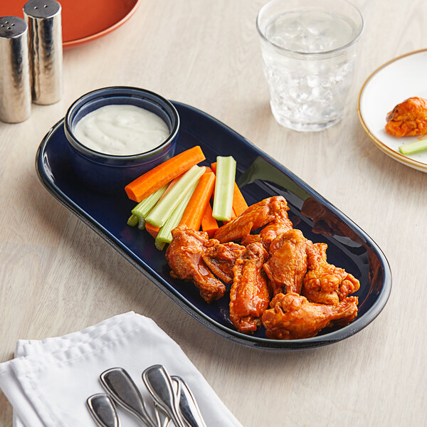 A table set with an Acopa Azora Blue stoneware oblong coupe platter with chicken wings and vegetables.