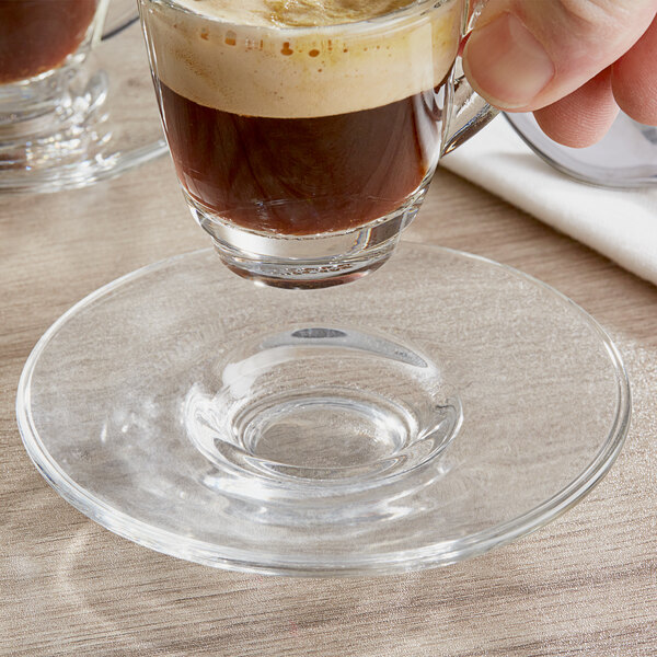 An Acopa espresso saucer with a glass of liquid on it.