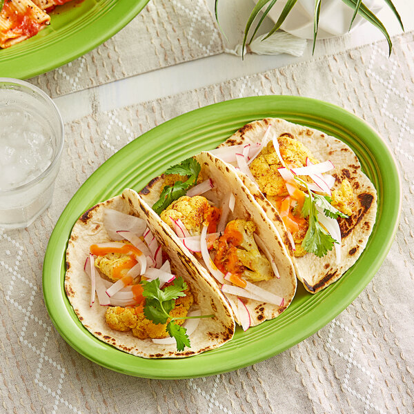 An Acopa Capri bamboo oval platter with tacos and vegetables on a table.