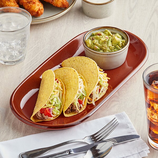 An Acopa Sedona orange stoneware oblong coupe platter with tacos and guacamole on a table.