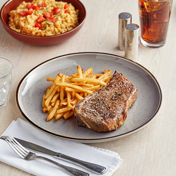 An Acopa Keystone granite gray stoneware coupe plate with steak and french fries on it on a table.