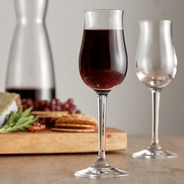 Two Stolzle port wine glasses filled with wine on a table next to a cutting board.