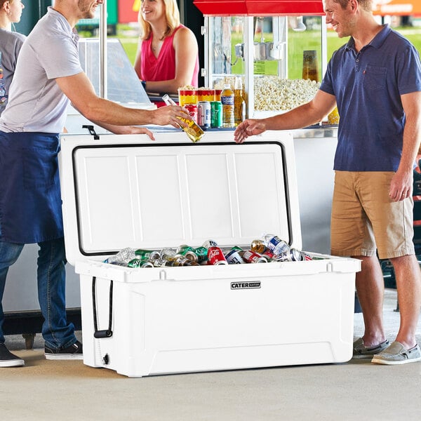 A group of people standing next to a white CaterGator outdoor cooler full of cans.
