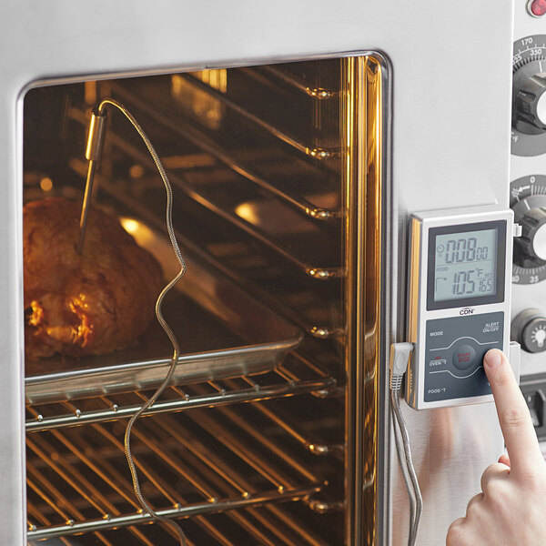 A person using a CDN digital thermometer to control the temperature of food in an oven.