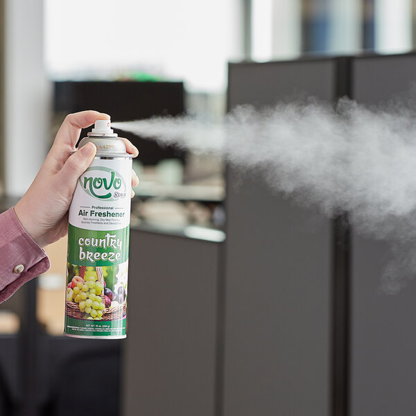 A hand holding a green and white aerosol can of Noble Chemical Country Breeze air freshener.