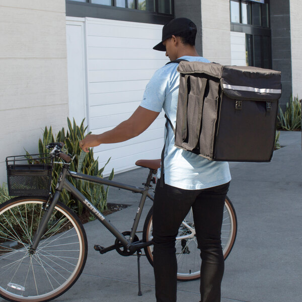 A man with a Cambro GoBag on his back standing next to a bicycle.