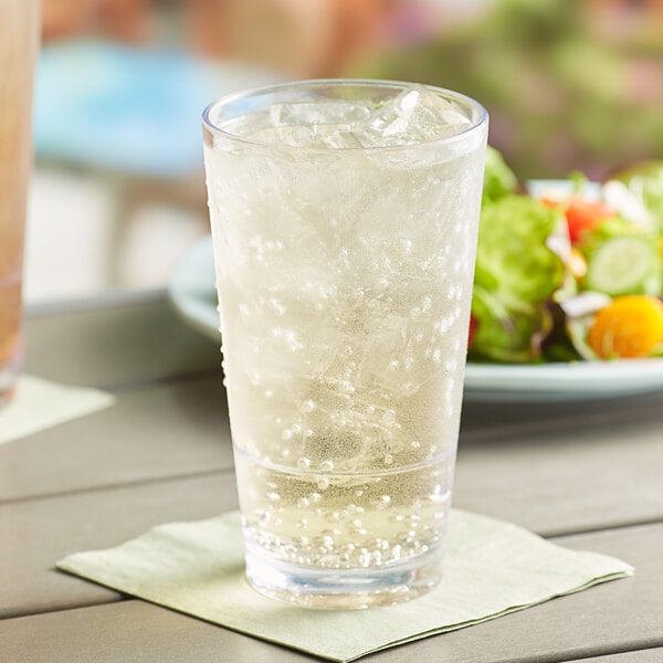 A Choice stackable plastic mixing glass filled with ice and soda on a table with a plate of salad.