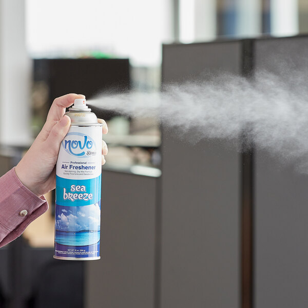 A person spraying a can of Noble Chemical Novo Sea Breeze air freshener.