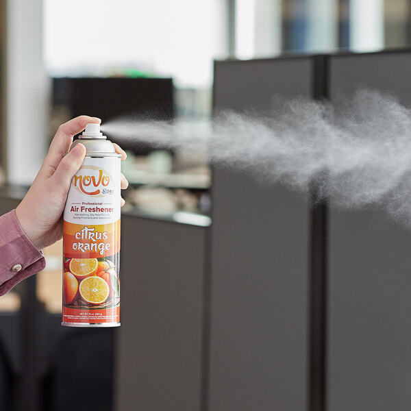 A person spraying a can of Noble Chemical Novo Citrus Orange air freshener