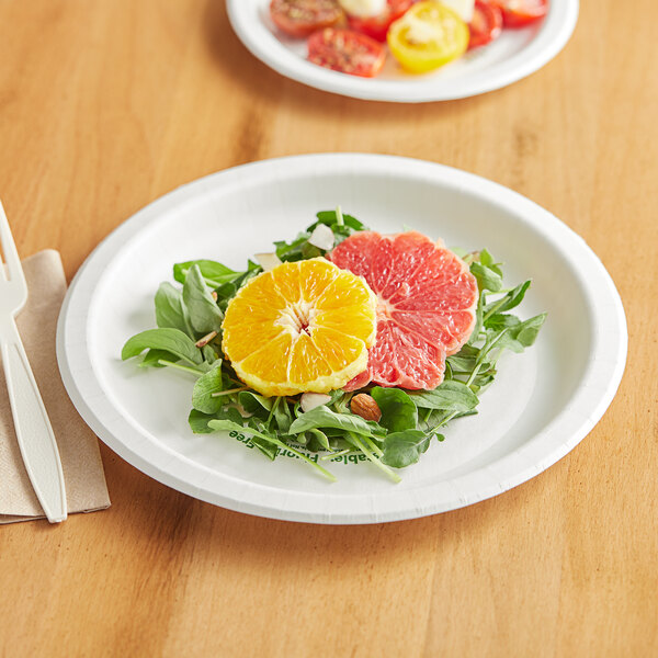 A Pactiv EarthChoice white compostable paper plate with orange slices and fruit on it on a table.