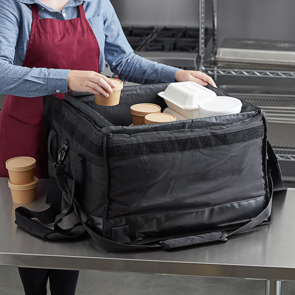 A woman in a red apron using a Vesture large black bag to hold containers of food.