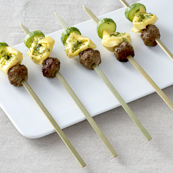 Bamboo flat skewers with meat and vegetables on a white plate.