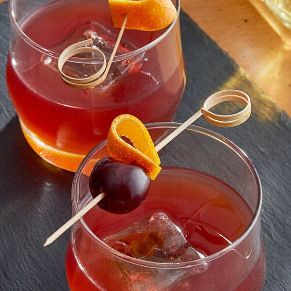 Two glasses of red liquid with orange slices and a cherry on a Bamboo Loop Skewer.