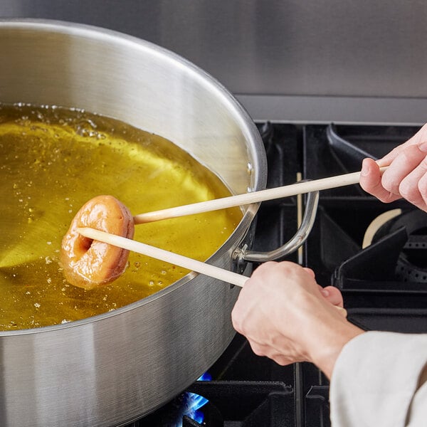 A person using an Ateco birch wood donut stick to cook a donut in oil.