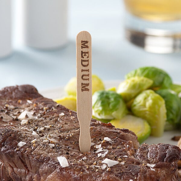 A piece of steak with a TreeVive by EcoChoice wooden stick in it next to vegetables.