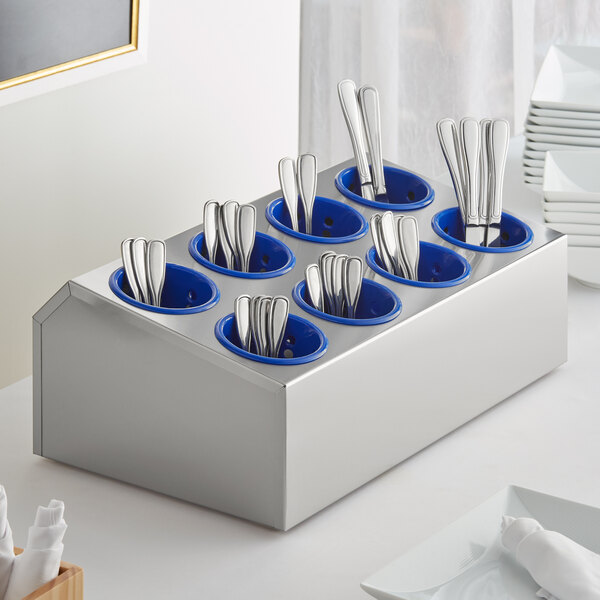 A stainless steel flatware organizer with blue plastic cylinders holding silverware.