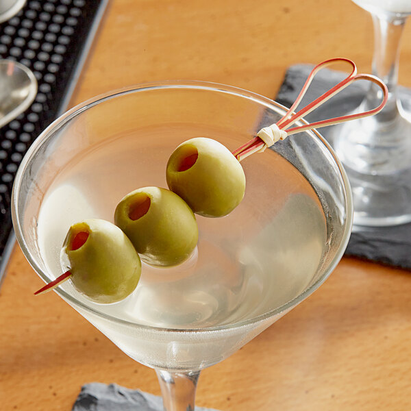 A martini glass with olives on red heart skewers.