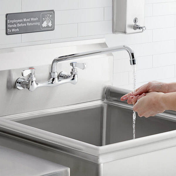 A person washing their hands under a Regency wall mount faucet over a stainless steel sink.