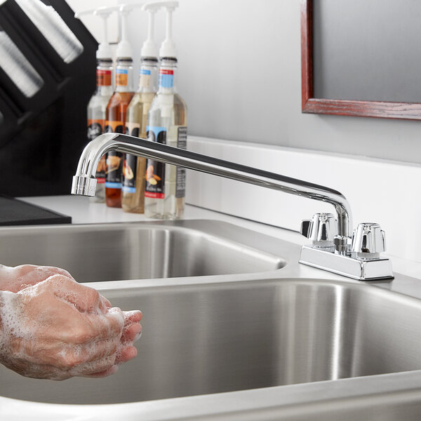 A person washing their hands in a professional kitchen sink using a Regency deck mount faucet.