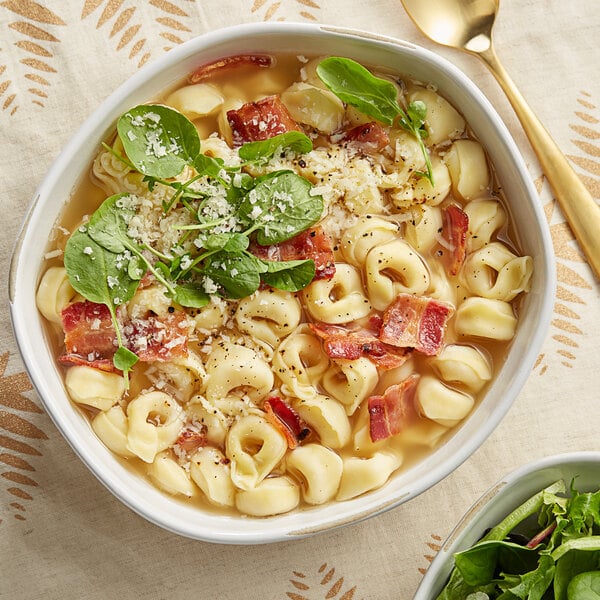 A bowl of soup with tortellini and cheese.