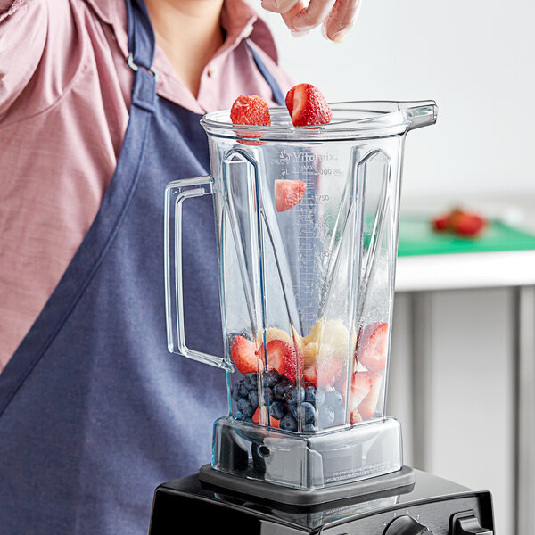 A woman in an apron pouring fruit into a Vitamix blender.