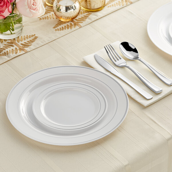 A white table setting with Visions banded plastic plates, silverware, and flowers.