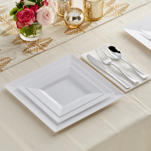 White plastic dinnerware and silver classic flatware on a table with flowers.
