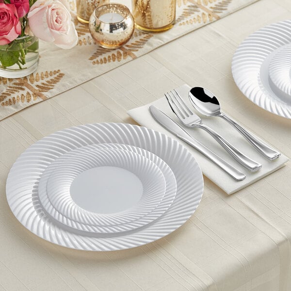 A white Visions plastic dinner plate with silver Classic flatware on it.