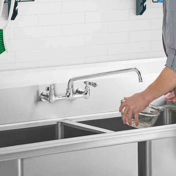 A person washing dishes in a sink with a 16" swing spout on a faucet.