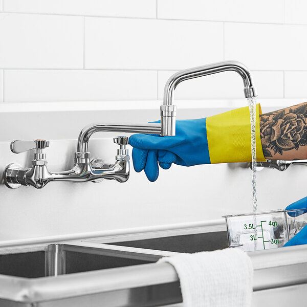 A person wearing blue rubber gloves uses a double-jointed swing spout to fill a measuring cup on a kitchen counter.