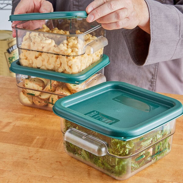 A woman holding a Carlisle clear plastic container of macaroni and cheese with a green lid.