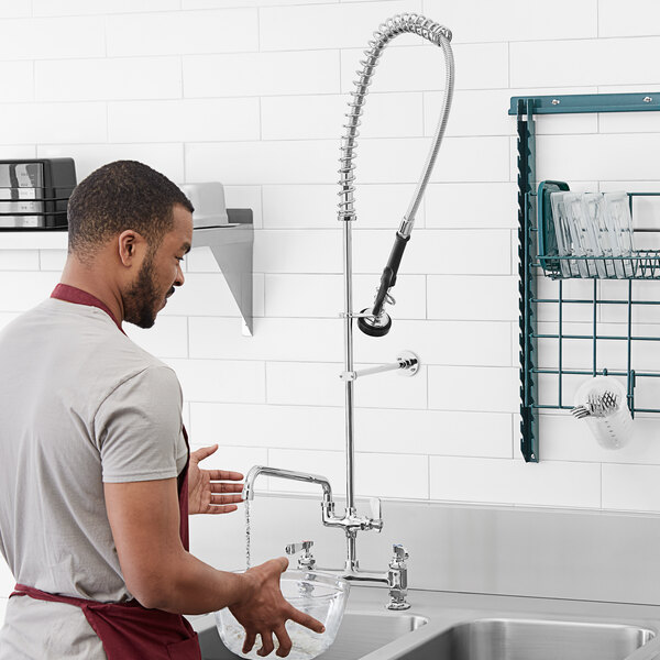 A man in a red apron using a Regency deck mount pre-rinse faucet on a sink.