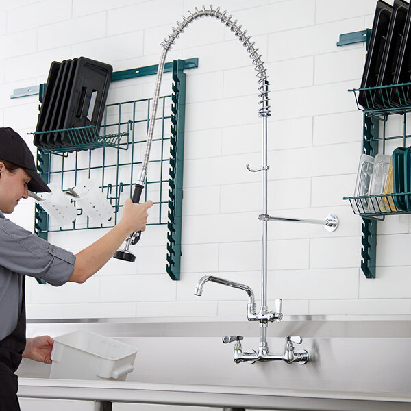A person using a Regency wall mount pre-rinse faucet over a sink.