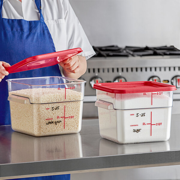 A person in a blue apron holding a Carlisle clear plastic container with rice and a red lid.