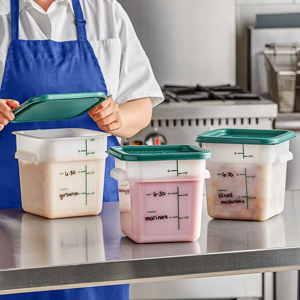 A person in a blue apron holding a green lid over a Carlisle white plastic food storage container.