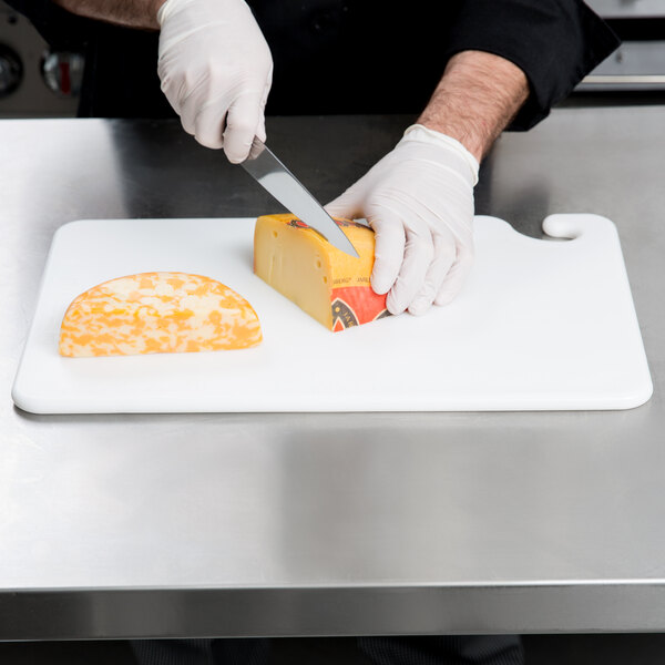 A person using a San Jamar white cutting board to cut cheese.