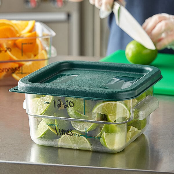 A person cutting limes in a Vigor clear polycarbonate food storage container on a counter.