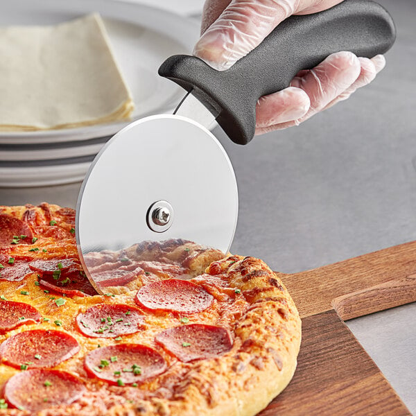 A person using a Choice 4" Pizza Cutter with a black handle to cut a pepperoni pizza.