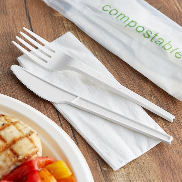 A white EcoChoice plastic fork and knife next to a plate of food.