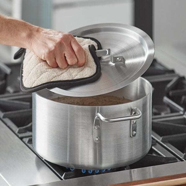 A hand holding a Choice aluminum sauce pot with a lid over a pot.