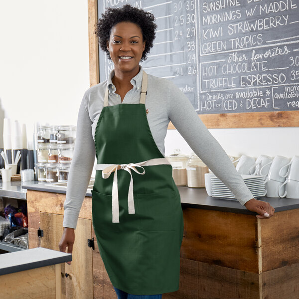 A woman standing in a green Choice bib apron with natural webbing accents.